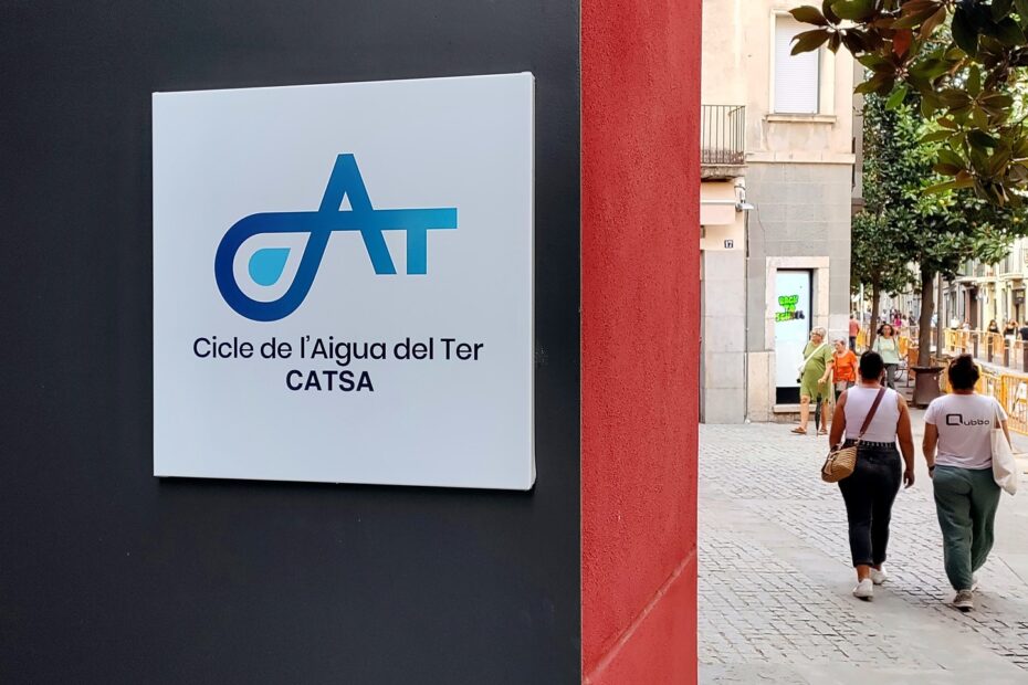 Placa amb el logotip de Cicle de l'Aigua del Ter (CATSA) a la façana d'un edifici, amb un carrer de vianants al costat