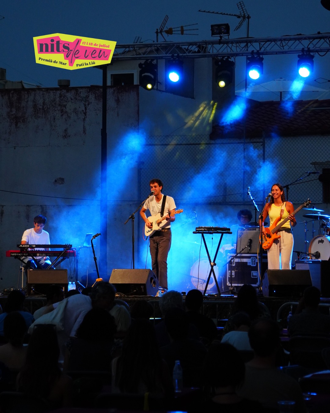 Un grup de música actua al capvespre a l'escenari del Pati la Lió, il·luminat amb focus blaus, davant del públic del festival Nits de Veu