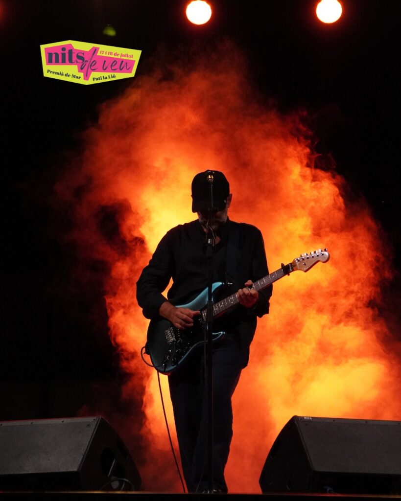 Un guitarrista amb gorra toca a contrallum davant d'una cortina de fum taronja a l'escenari del festival Nits de Veu, al Pati la Lió de Premià de Mar