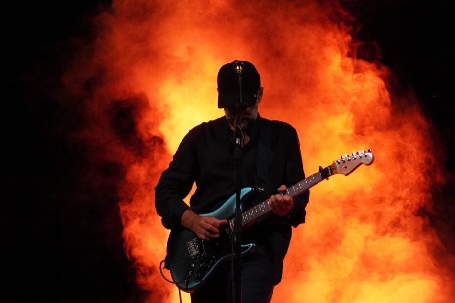 Un guitarrista amb gorra toca a contrallum davant d'una cortina de fum taronja a l'escenari del festival Nits de Veu, al Pati la Lió de Premià de Mar